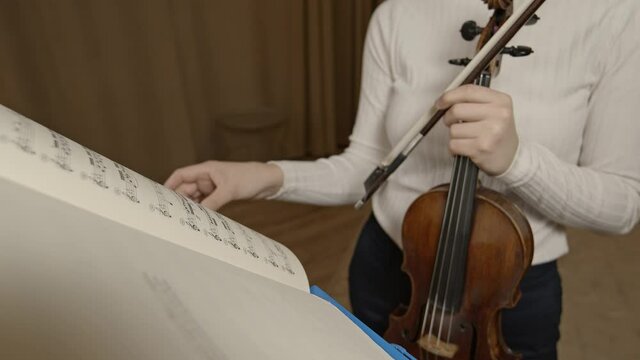 Female hand violinist flip through notes on music stand, background violin and bow. Gimbal shot of classical musician studying music notes, leaf through on a stand