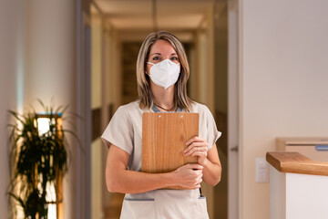 woman receptionist holding folder with documents and with mask in hospital