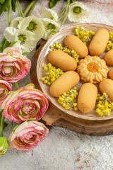 a plate of cookies on wooden platter and beautiful-colored flowers on marble background