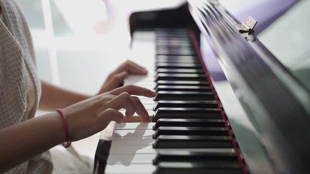 close up asian kid hand using fingers playing piano at home. child practicing two hands piano performance. 