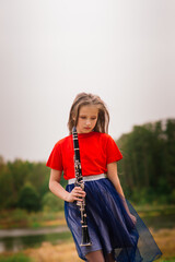 Young attractive girl playing clarinet, ebony in fall park