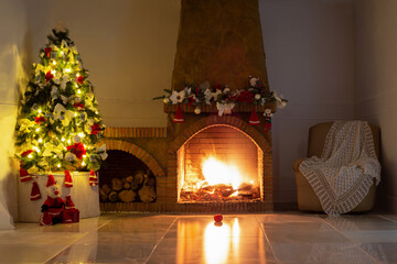 Christmas background with decorated christmas tree, bright lights, stone fireplace , natural fire, christmas tree garland, armchair with knitted warm cape on beige glossy marble floor with lights off