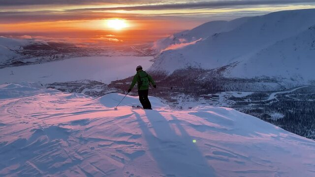 A man is skiing along a mountain ridge in the rays of the setting sun