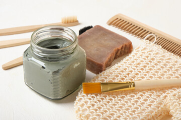 soap, blue clay in a glass jar, brush, washcloth and bamboo toothbrushes on a beige background,