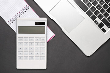 Modern calculator, notebook and laptop on dark background