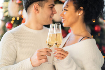 a young couple of friends hold glasses in their hands with a champagne drink and clink glasses. Christmas tree with toys is decorated for Christmas. celebrate the holiday of Christmas.