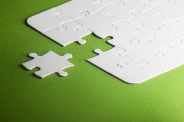 white puzzle with one piece missing but not fitting. green background. copy space