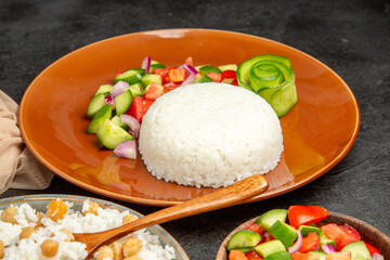 Half shot of homemade rice dishes salad with tomato and cucumber and towel on dark table
