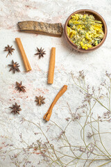 a bowl of dry bright yellow flower and cinnamon sticks and anice and dry herb on marble ground