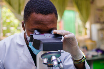 young handsome african scientist in the lab carefully carrying out experiments while using a...