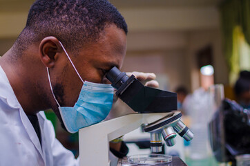 young handsome african scientist in the lab carefully carrying out experiments while using a...