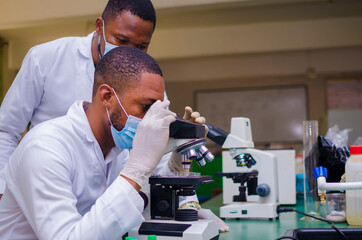 young handsome african scientist in the lab carefully carrying out experiments while his senior scientist help him out