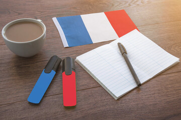 French national flag, pen, notebook, markers and coffee cup on wooden table, foreign language learning concept 