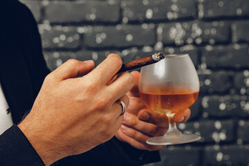 Man holding a glass of whisky and lit cigarette in hands close up