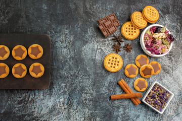 top view of cookies on wooden platter and chocolate bars and bowls of dry flowers on grey ground