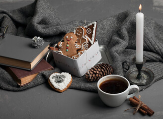 Christmas gingerbread cookies decorated with icing in a tin box and coffee in a cup. Against the background of a gray knitted woolen fabric. Candle. New Year's composition. Winter composition