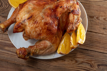 Close-up Whole fried chicken baked with oranges and carrots on a white dish on a brown wooden table.