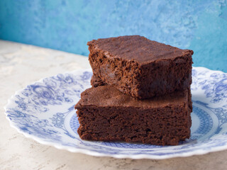 Appetizing brownie slices. Rustic tasty chocolate cake on a beautiful plate with a blue pattern on a gray and blue background. Delicate dessert with a rich chocolate flavor.