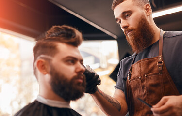 Cool barber grooming handsome client in salon