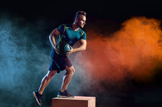 Attractive sportsman with medicine ball exercise in the fitness gym on the color smoke background. Copyspace area for advertise slogan or text message. Functional training and crossfit concept.