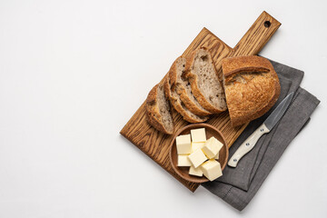 Sliced bread on cutting board and pieces of butter in wooden bowl on white background. Simple food breakfast