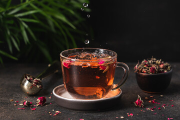 Water drops falling into flower tea. Fresh tea from rose petals. Pink hot drink on dark brown background