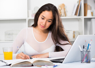 Young and smiling woman writing in notebook at home at the table