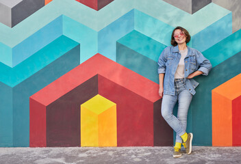 Cheerful young woman leaning on colorful wall
