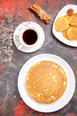 Above view of American homemade pancakes on a white plates and a cup of tea on mixed color table