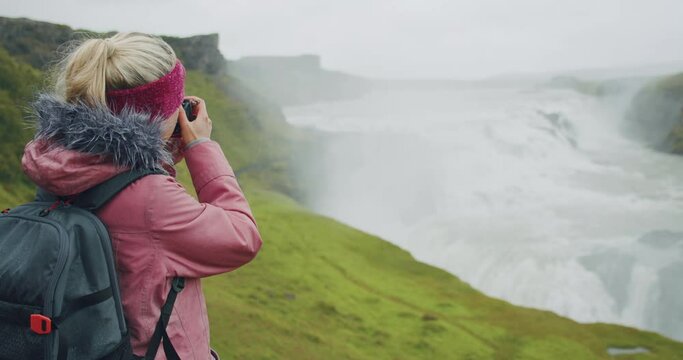 Tourist woman in rain photographing impressive Gullfoss waterfall. Famous attraction and landmark destination on Iceland on the Golden Circle