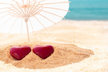 Two red hearts under beach umbrella, blue sky and sea in background. Valentines Day, 14 February symbol. Copy space