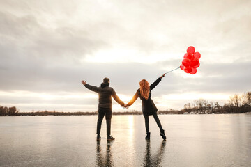 Love couple with red balloons outdoor in winter ice river. Sunset light, back view. Black casual clothes.