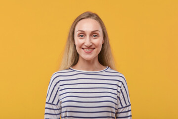 Portrait of a beautiful young blonde woman looking at the camera. Yellow background.