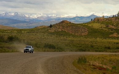 truck in the distance traveling on a dirt road with mountains in the background