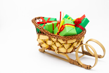 Old-fashioned wicker Santa sleigh with Christmas gifts wrapped in green paper with red ribbon