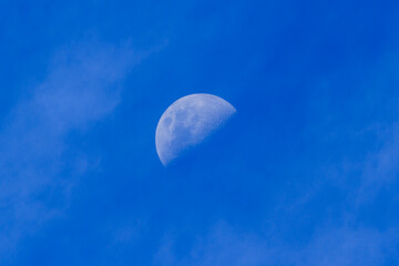 A half moon (first quarter) seen in a blue daytime sky with clouds. Photographed in the Southern...