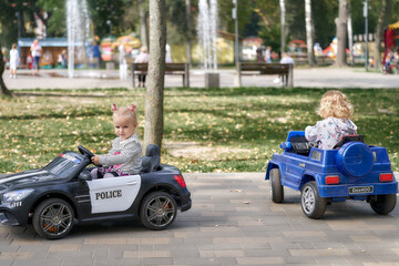 Two little girls in the park ride on children's electric cars.