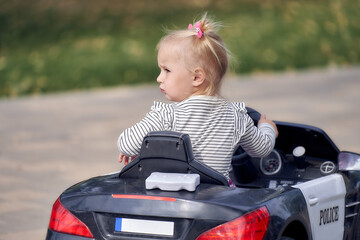 A little girl is riding a children's toy car without looking ahead.Weekend in the park.close-up.