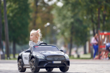 A little girl is riding a children's toy car without looking ahead. Weekend in the park.