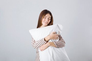 Fototapeta premium Beautiful young girl in a good mood in pajamas with a pillow in her hands on a light gray background