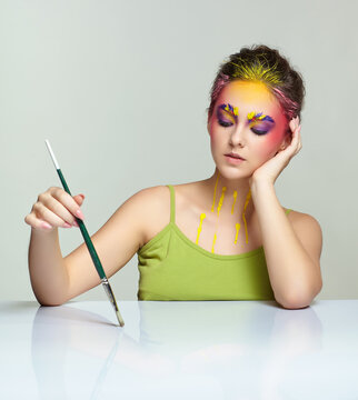 Portrait of young woman posing at the table with brush in hand.