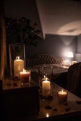Glass jar's with burning candles ligh the room, making a romantic and warm atmosphere in retro bedroom with nice decoration in background.