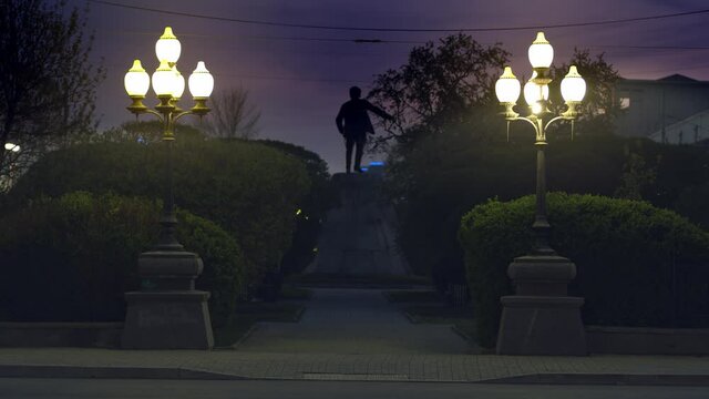 Rear view of a monument in the name of Yakov Sverdlov in ekaterinburg, Russia. Stock footage. Late evening in the street with green alley and street lanterns leading to the sculpture. 