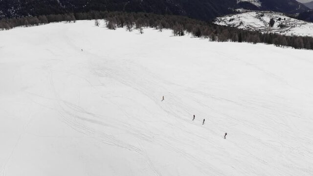 top aerial view of group of skiers skiing on empty ski slope in clouds of snow. top view tracking shot of good alpine skiers skiing down the wide ski slope together. Sunny winter day. slow motion