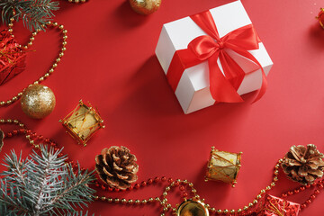 White box with padark and red bow around Christmas decorations with spruce branches on a red background