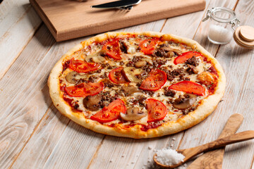 Side view on minced meat pizza with mushrooms and tomatoes on the wooden table