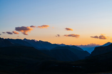Colorful dawn landscape with beautiful mountains silhouettes and golden blue gradient sky with clouds. Vivid mountain scenery with picturesque multicolor sunset. Scenic sunrise view to mountain range.