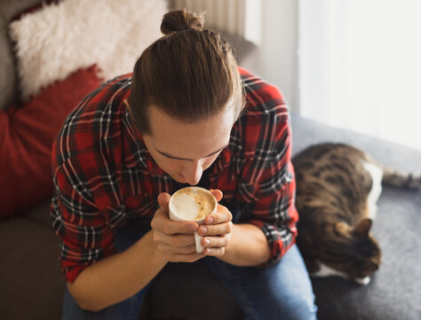 Young man enjoying coffee at home. Man with a cup of cappuccino sitting on the sofa with a cat