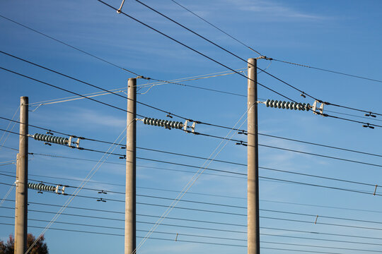 Concrete post power poles, insulators and high voltage wires and cables supplying city electrical energy against a blue sky.