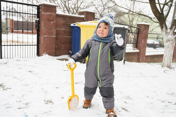 A cute toddler baby outdoors on snow background. Boy playing with a shovel outdoors. Little helper concept.